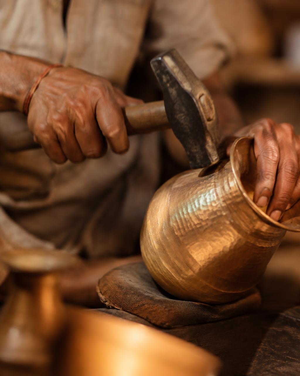 Artisan hammering a brass vessel